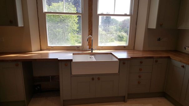 A new kitchen being installed with a belfast sink centered between uPVC windows